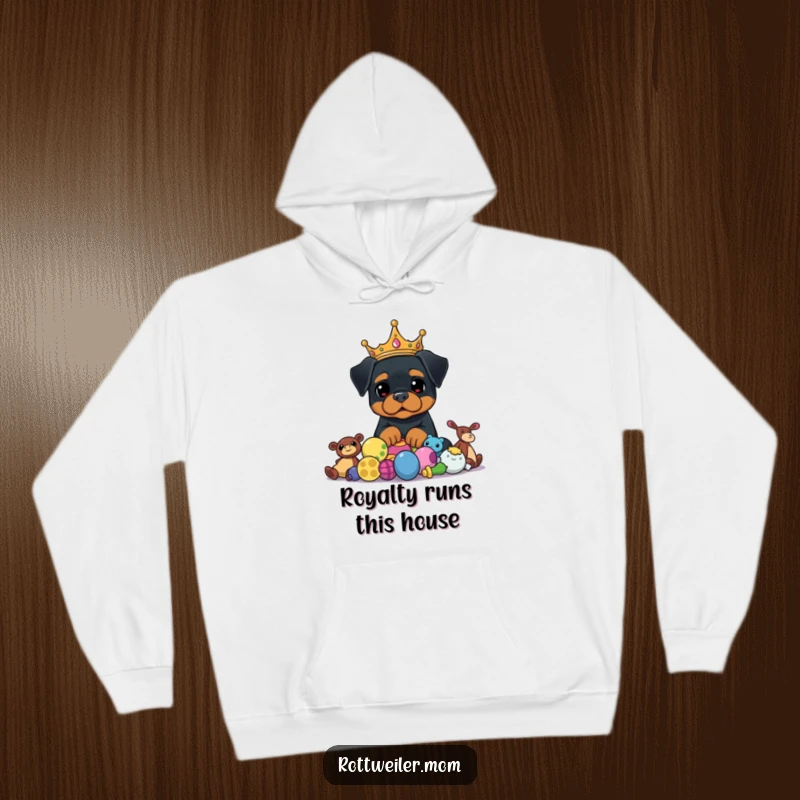 Funny Rottweiler King Hoodie shows a majestic dog wearing a crown, sitting proudly above a mountain of dog toys, looking hilarious.
